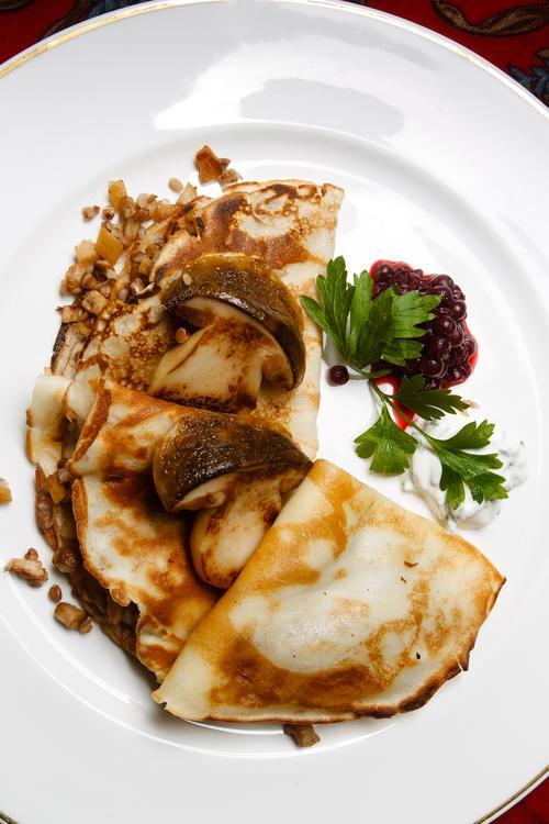 Фотография пленит взгляд изысканными блинами, воплощая в себе вкус и традиции русской кухни. Этот кулинарный момент отражает атмосферу праздника Масленицы, где за столом царит уют и тепло семейного собрания. Изображение идеально подходит для кулинарных изданий, гастрономических блогов, а также может использоваться в рекламе продуктов, призывая к наслаждению великолепными вкусами и традиционной русской кулинарией.